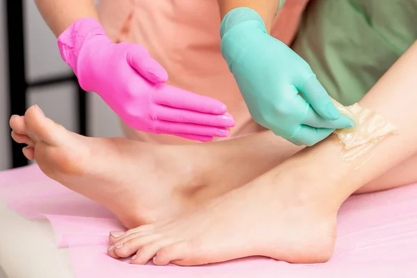 Hands in gloves waxing legs of woman while epilation process close up.