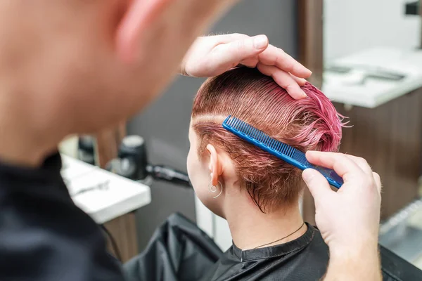 理发师正在美发店里用梳子梳理女性的粉色头发 男人的手正在美容院梳理女人的短粉色头发 靠近点 — 图库照片