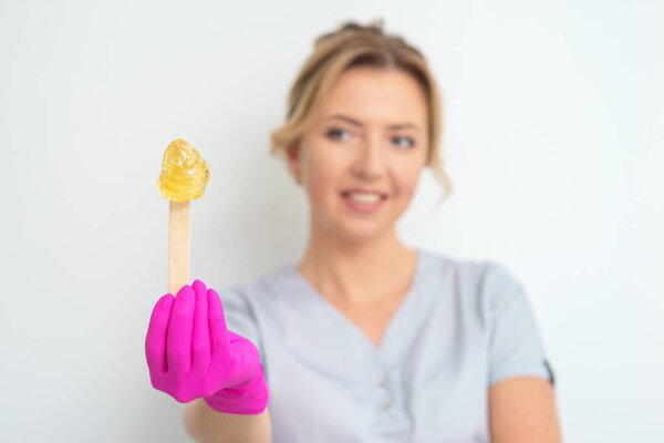 Stick with wax for epilation in beautician's hand on white background.