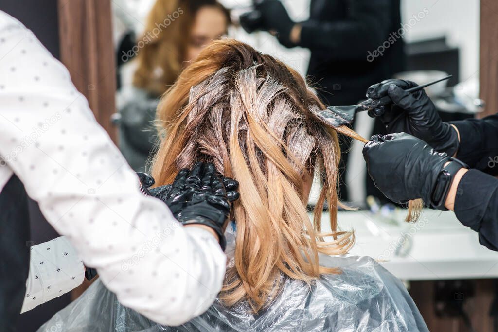 Hairdresser in black gloves is dyeing a woman's hair. Hairdresser is applying color cream at hair. Painting hair.