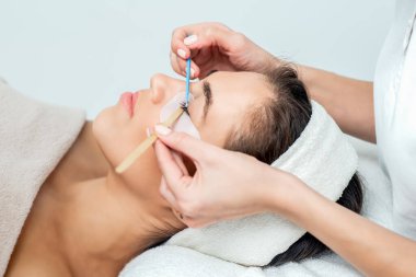 Kozmetikçinin eli pamuk tomurcuğunun yardımıyla kirpiklerini uzatıyor..