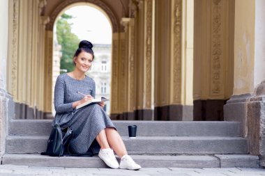 Genç üniversite öğrencisi kız merdivenlerde kitap okuyor. Öğrenci kız, üniversite binasının merdivenlerinde kitap okuyor..