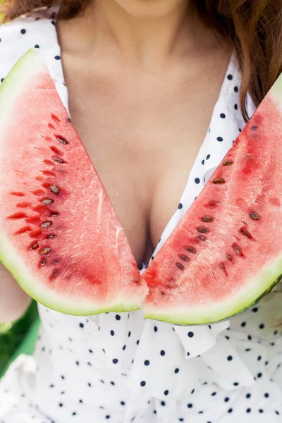 Two pieces of watermelon covers chest of young woman close up. Female in white dress with two slices of watermelon.