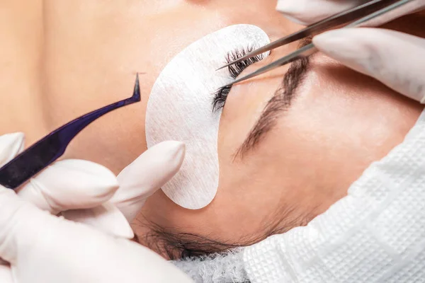 Procedure of eyelashes extension in salon on woman eye with long eyelashes during eyelash extension.