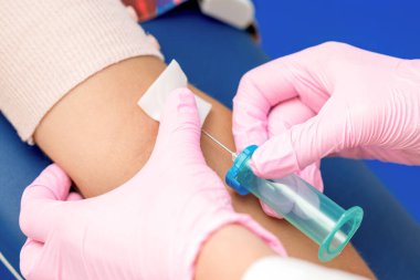 Hemşire kan örneği alır ve kadının koluna iğne batırır..