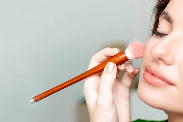 Makeup artist applies skin tone on face of woman with copy space.