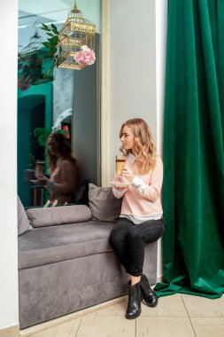 Kanepede kahve içen genç ve güzel bir kadın pencereden içeri bakıyor..