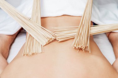 Dört elle masaj yaparken genç bir adamın sırtındaki bambu süpürgeleri..
