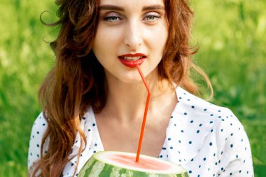 Dışarıda çimlerin üzerinde oturan karpuz tutan güzel genç bir kadının portresi..