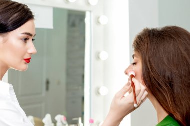 Profesyonel makyöz, güzellik salonunda genç ve güzel bir kadın için yanaklarına pudra sürüyor..