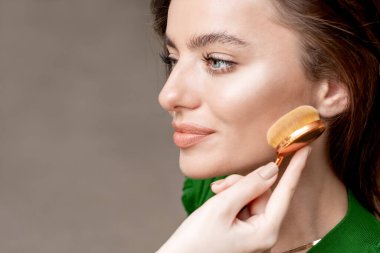 Makyaj sanatçısı yüzüne makyaj fırçası sürüp makyaj malzemesi sürerek makyaj malzemesi yapıyor..