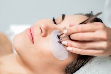 Kozmetik uzmanı, takma kirpiklerini kadının gözüne cımbızla yapıştırırken kirpik uzatma prosedürü uyguluyor..