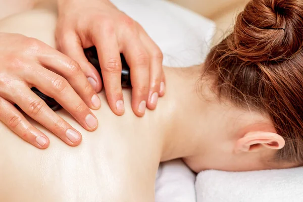 Hands of massage therapist doing back massage with massage stones on back of woman close up.