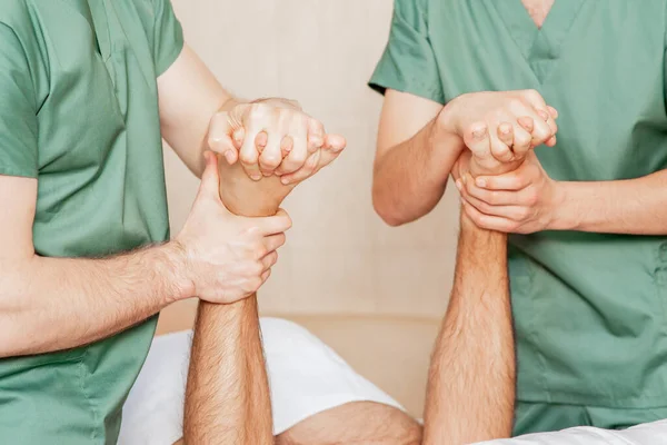 Man receiving toe massage by two male massage therapists.