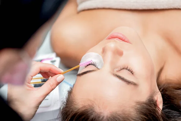 Cosmetologist hand does eyelash extension with eyelash brush close up.