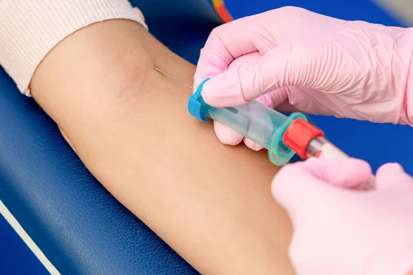 Nurse takes blood sampling introducing a needle into a vein of woman\'s arm.