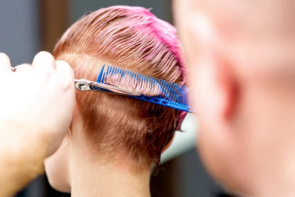 Hands of hairdresser cuts hair of woman close-up and back view.