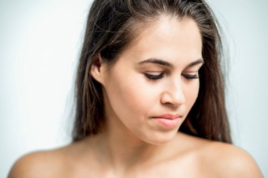 Güzel bir genç kadının portresi uzun siyah saçları ve çıplak omuzlarıyla aşağıya bakıyor..