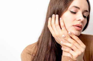 Güzel genç bir kadının beyaz arka planda bej rengi manikürle yüzüne dokunan portresi..