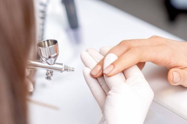 Manikür ustası, tırnaklarını bej rengine boyuyor. Tırnak manikürü yaptıran kadın..