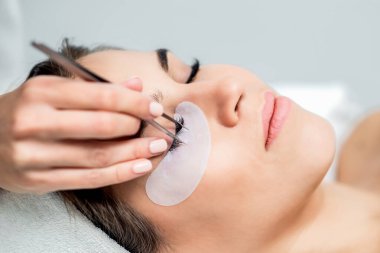 Kozmetik uzmanı, kirpik uzatma işlemi sırasında kirpikleri kadının gözüne cımbızla ayırıyor..