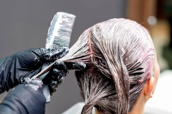 Hands of hairdresser are dyeing hair of woman, close up.
