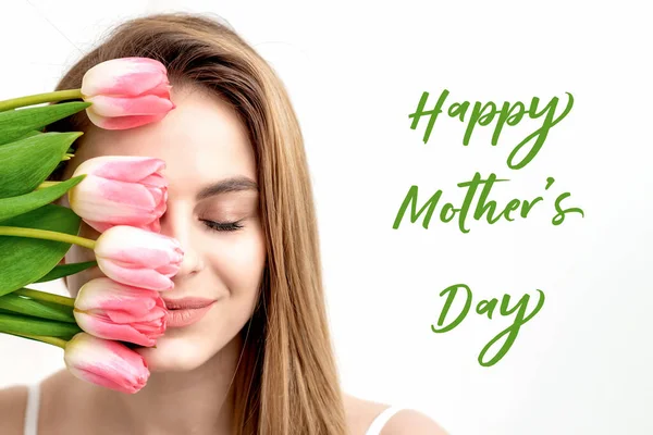 幸せな母の日の緑のテキストのサインと白の背景にピンクのチューリップと若い女性の肖像画 花を持つ若いお母さん — ストック写真