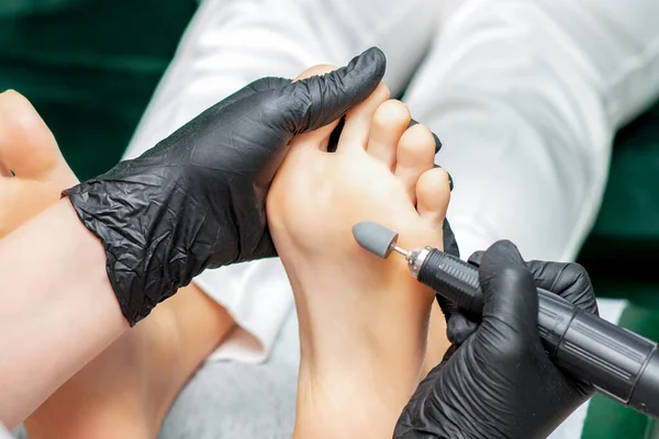 Pedicure master is polishing foot of woman with special machine tool, close up.