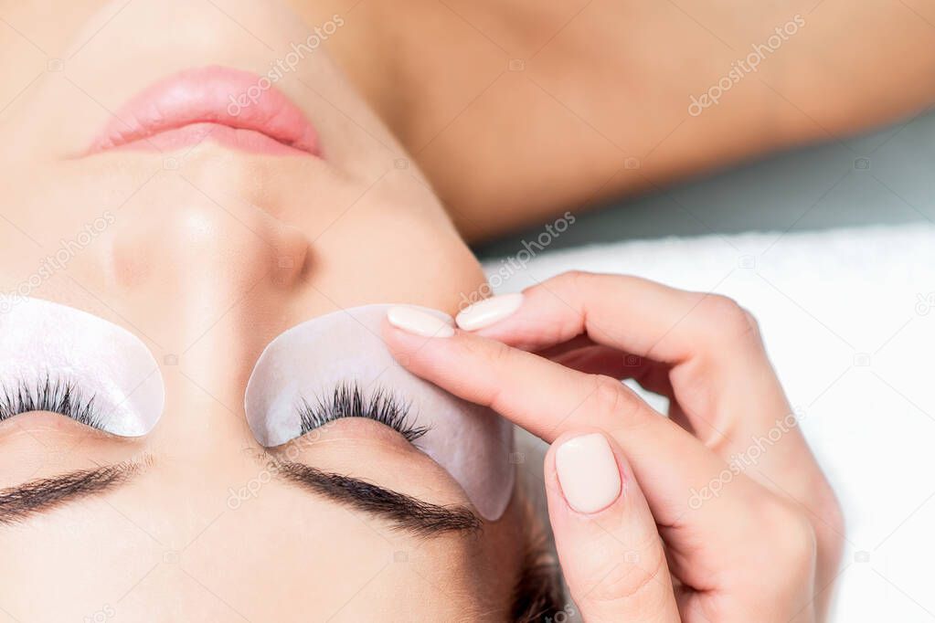 Cosmetologist hand glue duct tape under eyes of young woman face before eyelash extension procedure, top view.