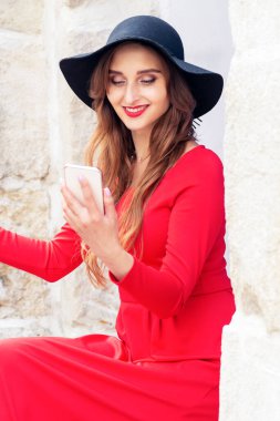 Kadın şehirde kırmızı elbise ve siyah şapka giyerek selfie çekiyor..
