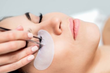 Kozmetik uzmanı, kirpik uzatma işlemi sırasında kirpikleri kadının gözüne cımbızla ayırıyor..