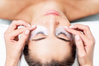 Kozmetik uzmanı, kirpik uzatma prosedüründen önce genç bir kadının gözlerinin altına koli bandı yapıştırıyor..