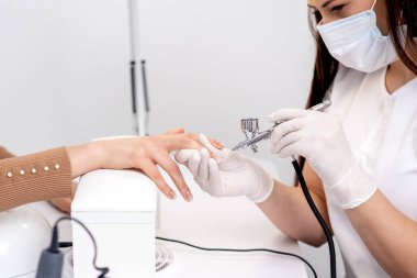 Manikür ustası, tırnaklarını bej rengine boyuyor. Tırnak manikürü yaptıran kadın..