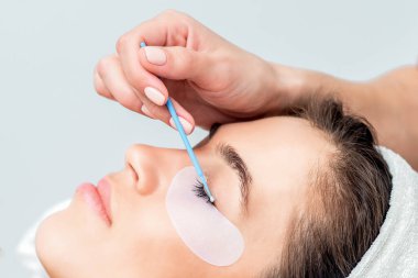 Hand of cosmetologist wipes eye of woman by cotton bud. clipart