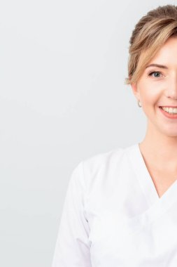 Yarı yüz güzel doktor, stajyer ya da beyaz cüppeli kozmetik uzmanı portresi beyaz arka planda izole bir şekilde kameraya gülümsüyor..