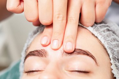 Kozmetik uzmanının parmakları tarafından alnına masaj yapılan güzel bir kadın..