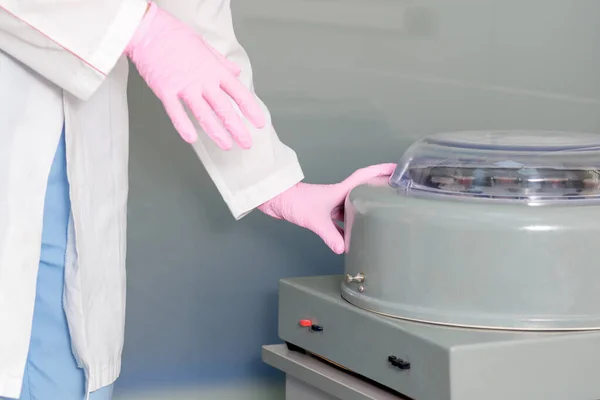 Doctor hands is using centrifuge machine wearing gloves in medical lab.
