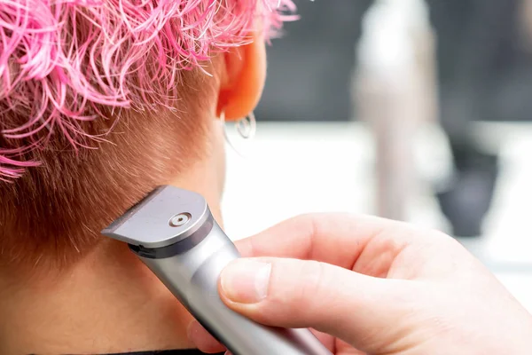 理发师的手正在理发 用电动修发机在美发厅里给一个女人剃光粉色的头发 — 图库照片