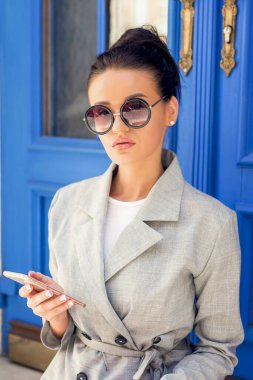 Avrupa 'da akıllı telefon kullanan güneş gözlüğü takan bir kadın. Şehrin güzel kızı kapıya yakın..
