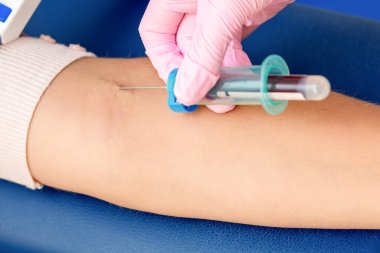 Hemşire kan örneği alır ve kadının koluna iğne batırır..