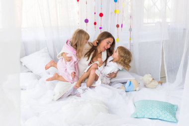 Evde iki kızıyla yatakta oynayan genç bir kadın. Evde ve aile kavramında kal.