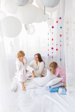 Evde iki kızıyla yatakta oynayan genç bir kadın. Evde ve aile kavramında kal.