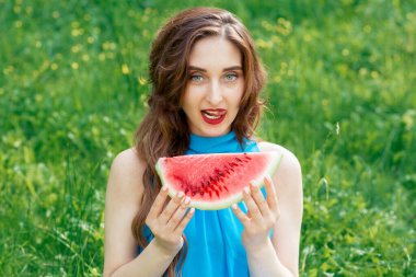 Güzel, seksi bir kadın elinde yeşil çimlerin arka planında bir dilim karpuz tutuyor..