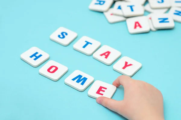 Child hand is making word STAY HOME with gaming letters on blue background.