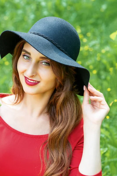 笑顔若い女性は緑の草の背景に黒い帽子を身に着けている三角形の形でスイカの作品を保持 — ストック写真