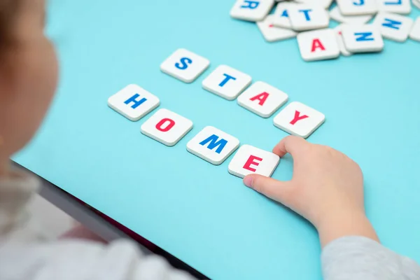 Child hand is making word STAY HOME with gaming letters on blue background.
