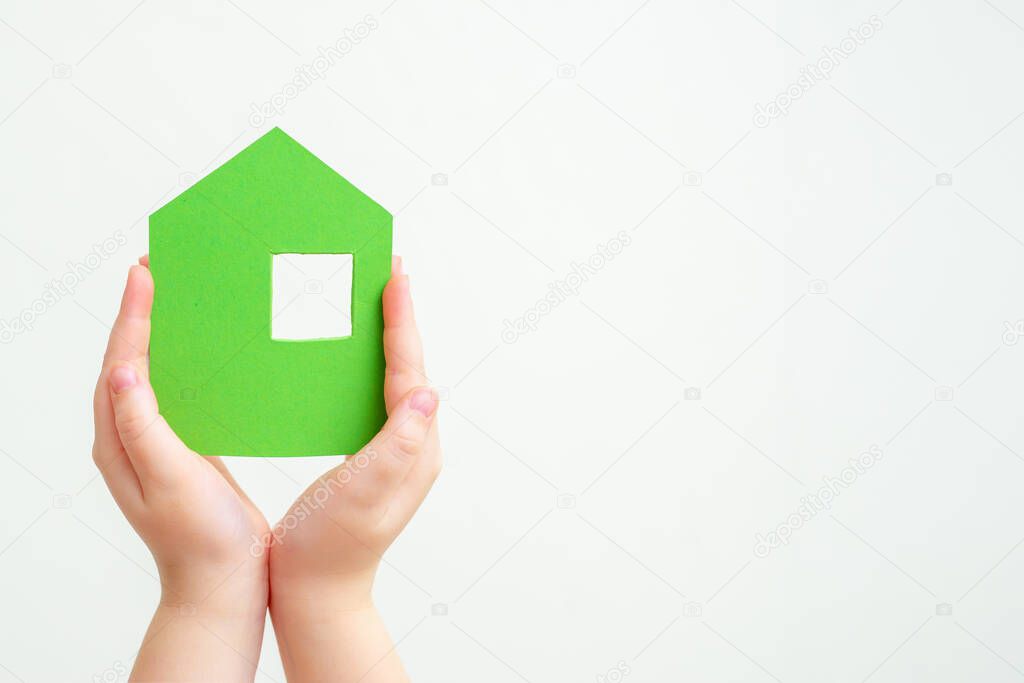 Children's hands holding a green paper house on a white background.