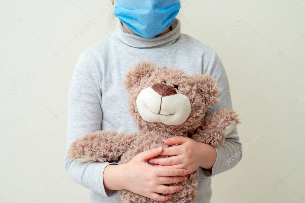 Child is holding Teddy bear wearing protective medical mask on white background. Health care and virus protection concept.