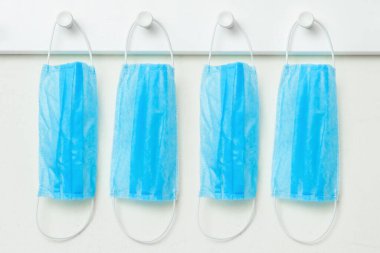 Beyaz duvardaki koronavirüs korumasından dolayı askıda asılı duran tıbbi maskeler. Virüs koruma kavramı.