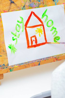 Çocuğun eli kırmızı evi çiziyor ve evde suluboya resim sehpasıyla evde kalıyor. Çocukların yaratıcılık kavramı.